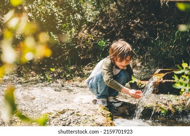 School boy kid drinking water from the mountain creek. Tourist child wearing casual clothes making a sip of mountain river water from the palms of his hands when hiking. - Shutterstock ID 2159701923