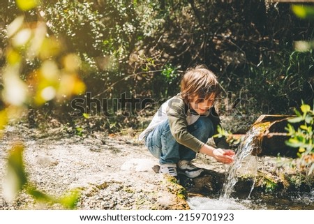 School boy kid drinking water from the mountain creek. Tourist child wearing casual clothes making a sip of mountain river water from the palms of his hands when hiking.
