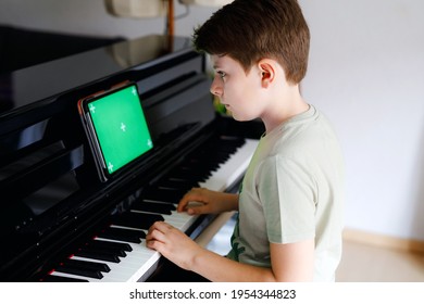 School boy learning play piano with tablet app. Child having fun with learning to play music instrument. Tablet with green screen chroma key background for new app, commerce and programs - Powered by Shutterstock