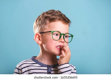 School Boy Nervously Biting Nails. Bulling And Childhood Psychology Concept, Child Boy In Uniform, Glasses And Backpack Isolated On Blue. Kid Portrait With Finger In Mouth