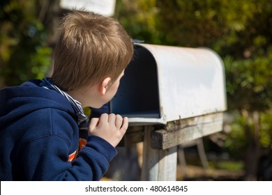 School boy opening a post box and checking mail. Kid waiting for a letter, checking correspondence and looking into the in the metal mailbox.