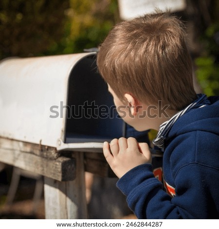 School boy opening a post box and checking mail. Kid waiting for a letter, checking correspondence and looking into the in the metal mailbox.