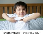 School boy sitting in bed and try to wearing his cloth with smiling face,Cute kid boy getting dressed and get ready for school,Child dressing uniform in bed room ready to school,Back to school concept