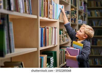 school boy taking books from shelves in library, with a stack of books in hands. child brain development, learn to read, cognitive skills concept - Powered by Shutterstock