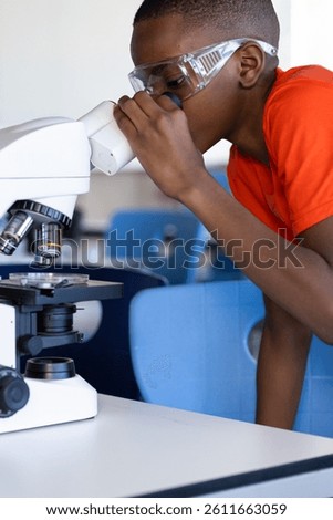 In school, boy using microscope and wearing safety goggles in science classroom. education, laboratory, teaching, learning, childhood, experiment