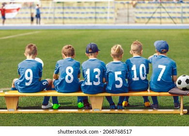 School Boys in Sports Football Team. Kids is Classic Blue Soccer Jersey Uniforms With Numbers. Kids Playing Sports Together. Children Sitting on Sideline Wooden Substitiute Bench - Powered by Shutterstock