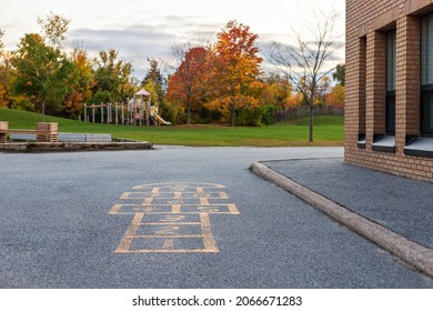 School building and schoolyard with playground for children in evening in fall season. Selective focus on hopscotch. Back to school educational concept