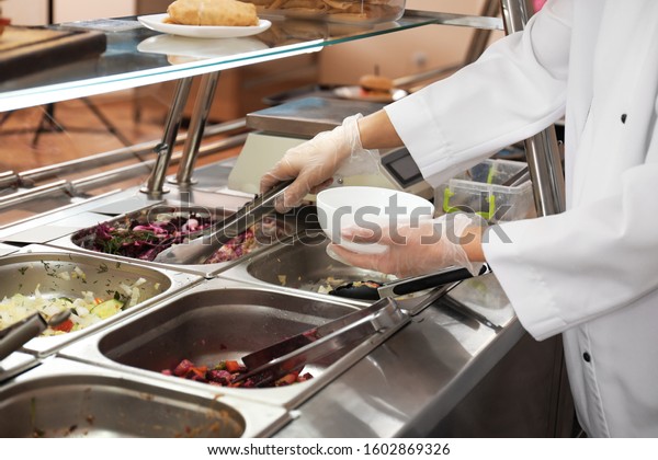 School canteen worker at serving line, closeup.\
Tasty food