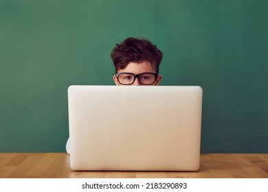 School child (boy) in classroom. Funny kid against green chalkboard in front of the laptop. Idea and creativity concept. Copyspace on background. Back to school concept.  - Shutterstock ID 2183290893