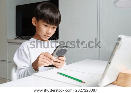 School child checking a smartphone while studying with a tablet and notebook at home. Modern learning environment combining mobile devices, schoolwork and digital technology.