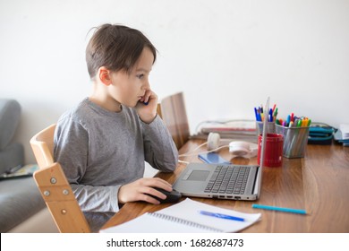 School child, sitting at the table with laptop, writing school tasks while homeschooling, while school closed due to Coronavirus