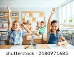 School children in classroom at lesson. Little children raising hands up and having fun in class.