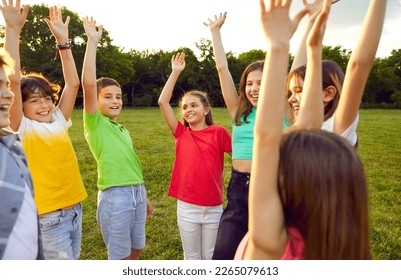 School children enjoy summer break, meet in the park, play games and have fun all together. Bunch of happy, joyful, excited friends standing on a green meadow, smiling and raising their hands up - Shutterstock ID 2265079613