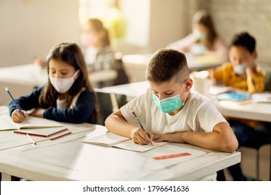 School Children With Face Masks Writing While Doing An Exam On A Class In The Classroom. 