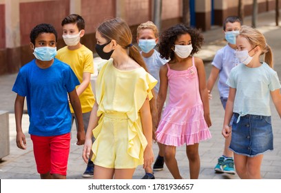 School Children In Protective Medical Masks Walk Along The Street Of A Summer City