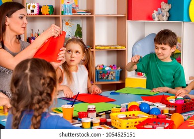 School children with scissors in kids hands cutting paper with teacher in class room. Group of children in an orphanage. Children's project in kindergarten. School origami exhibition.