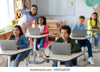 School children using laptops, female teacher pointing at blackboard during exam test at computer science class. Modern education - Powered by Shutterstock