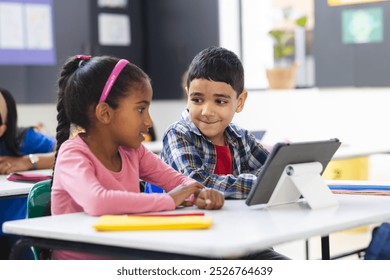 In school, in class, biracial female student and her brother look at a tablet. Both have dark hair and eyes, and she wears a pink headband, learning, education, unaltered - Powered by Shutterstock