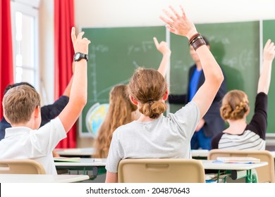 School class teacher giving lesson in front of a blackboard or board teaching students or pupils, they are raising their hands as they know all the answers - Shutterstock ID 204870643