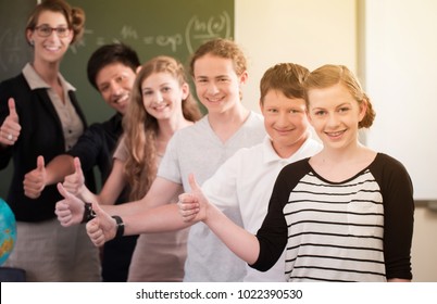 School Class Teacher And Students Stand In Front Of A Blackboard With Math Work In A Classroom During Lesson