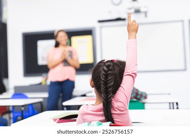 In school, in classroom, biracial young woman teaching, young girl raising hand. Both have dark hair, woman holding recycle poster, unaltered - Powered by Shutterstock