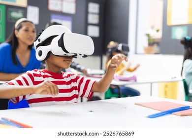 In school, in the classroom, a diverse group is exploring virtual reality, copy space. A middle-aged biracial female teacher watches a young African American boy using a VR headset, unaltered - Powered by Shutterstock