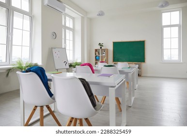 School classroom. Interior of spacious classroom at new modern school. Back to school. Clean empty room with white walls, big windows, comfortable desks, chairs, green chalkboard, whiteboard - Shutterstock ID 2288325459