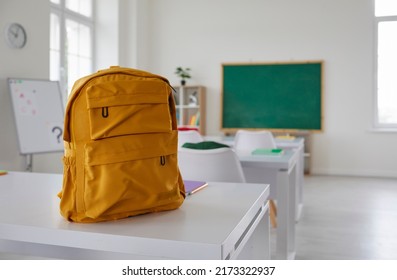 School classroom. New school bag on a student's desk in the classroom. Big yellow canvas backpack placed on the table in a large modern schoolroom with a chalkboard. Back to school concept