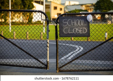 school closed sign with protective mask hanging on a padlocked gate, school closed or shutdown concept amid coronavirus fears and panic over contagious virus spread of the pandemic outbreak