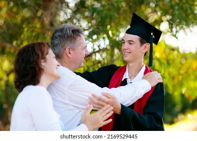 School Or College Graduation Ceremony. Young Man In Gown And Cap, With His Family. Moher And Father Cheer At Celebration Of Successful Diploma Certificate. High School Graduate In Robe And Mortarboard