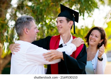 School Or College Graduation Ceremony. Young Man In Gown And Cap, With His Family. Moher And Father Cheer At Celebration Of Successful Diploma Certificate. High School Graduate In Robe And Mortarboard