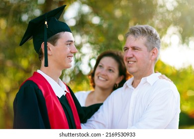 School Or College Graduation Ceremony. Young Man In Gown And Cap, With His Family. Moher And Father Cheer At Celebration Of Successful Diploma Certificate. High School Graduate In Robe And Mortarboard