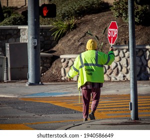 A School Crossing Guard Holding A Red Stop Sign While Walking Accross A Street