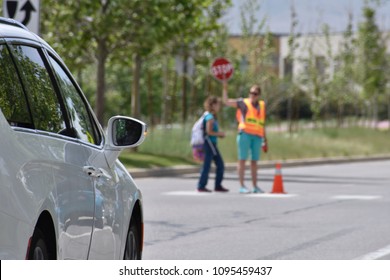 A School Crossing Guard Walks A Student Across A Crosswalk Holding A STOP Sign