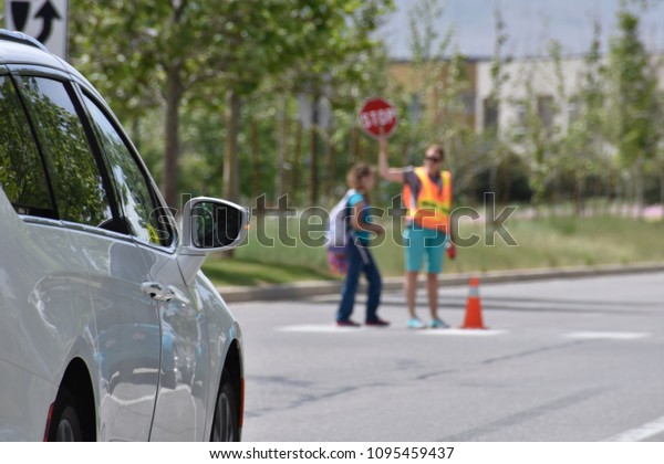 A school crossing guard walks a student across\
a crosswalk holding a STOP\
sign