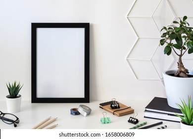 School Desk Against An Empty White Wall. Copy Space. Office Supplies. Plants In Pots, Geometric Texture And Glasses. Black Frame Mockup.