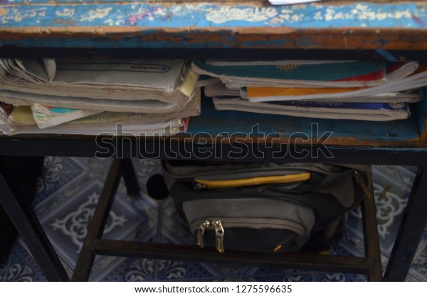 School desk filled with books in the space\
saver beneath the top, as well as a school back placed unter the\
table, in vintage\
atmosphere