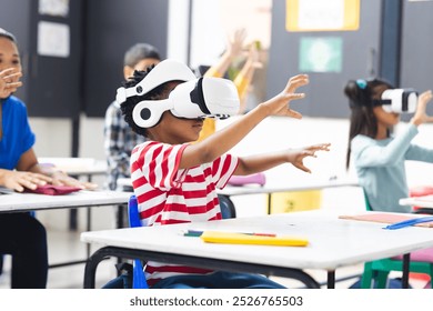 In school, diverse students wearing virtual reality headsets are reaching out in the classroom. They have dark hair, and the classroom is colorful with posters, unaltered. - Powered by Shutterstock