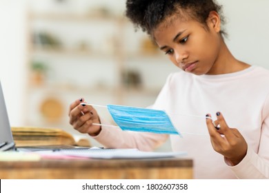 School During Pandemic. Black Teen Girl Holding Protective Mask Sitting At Desk Indoors. Selective Focus