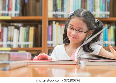 School Education And Literacy Concept With Asian Girl Kid Student Opening And Reading Children's Picture Book Happily In Library Or Classroom