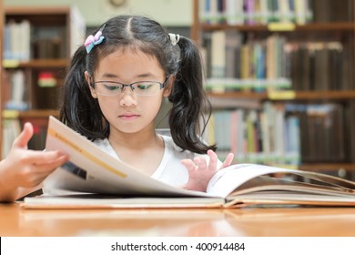 School Education And Literacy Concept With Young Asian Girl Student, Smart Kid In Elementary Grade Learning, Studying Hard Or Reading Children's Picture Book In Library Or Classroom