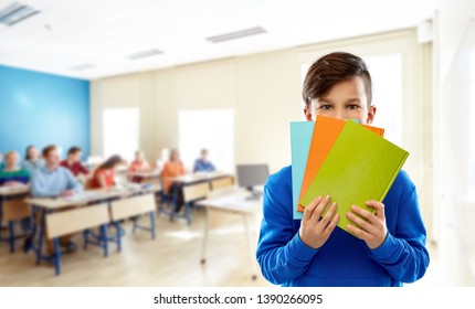 School, Education And People Concept - Shy Student Boy Hiding Behind Books Over Classroom Background