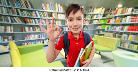 School, Education And People Concept - Smiling Little Student Boy In Red Polo T-shirt In Glasses With Books And Bag Showing Ok Hand Sign Over Reading Room Of Library Background