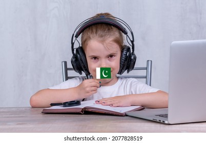 School Female Child With Pakistan Flag. Child In Headphones, With A Book And Laptop Has Lesson Online