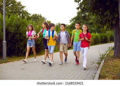 School friendship. Funny schoolchildren group with backpacks have fun walking together on path in park. Cheerful boys and girls in summer casual clothes return home from school lessons together.
