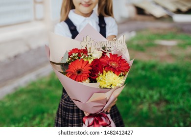 School Girl Dressed In School Uniform Holding A Bright Pink Festive Bouquet Of Beautiful Flowers For Teacher. No Face. Blurred Background.