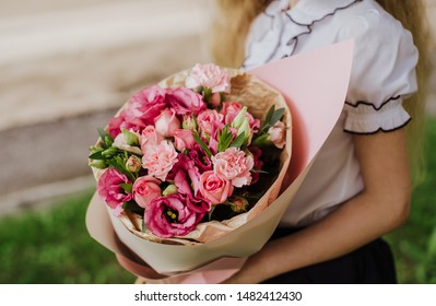 School Girl Dressed In School Uniform Holding A Bright Pink Festive Bouquet Of Beautiful Flowers For Teacher. No Face. Blurred Background.