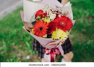 School Girl Dressed In School Uniform Holding A Bright Pink Festive Bouquet Of Beautiful Flowers For Teacher. No Face. Blurred Background.