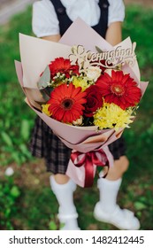 School Girl Dressed In School Uniform Holding A Bright Pink Festive Bouquet Of Beautiful Flowers For Teacher. No Face. Blurred Background.