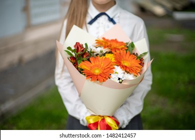 School Girl Dressed In School Uniform Holding A Bright Pink Festive Bouquet Of Beautiful Flowers For Teacher. No Face. Blurred Background.